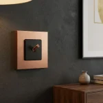 Brass light switches and sockets: a square brass plate with a black inset and a small lever switch on a dark wall.