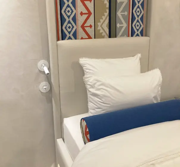Decorative headboard with colourful geometric panel, white pillows, and a blue bolster on a white bed. Decorative headboard with colourful geometric panel, white pillows, and a blue bolster on a white bed.