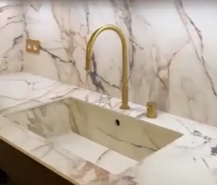 Brass faucet and matching brass controls above a marble sink with grey veining.