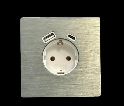 Brushed metal square wall plate with a circular European power socket in the centre and two small angled USB-style slots above. Brushed metal square wall plate with a circular European power socket in the centre and two small angled USB-style slots above.