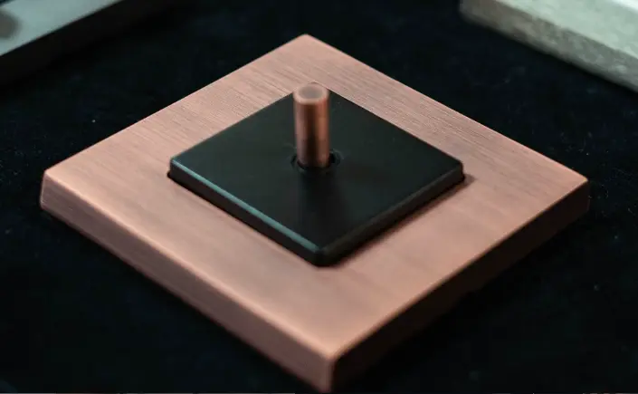 Copper square wall plate with a black inset square and a small copper cylindrical knob in the centre. Copper square wall plate with a black inset square and a small copper cylindrical knob in the centre.
