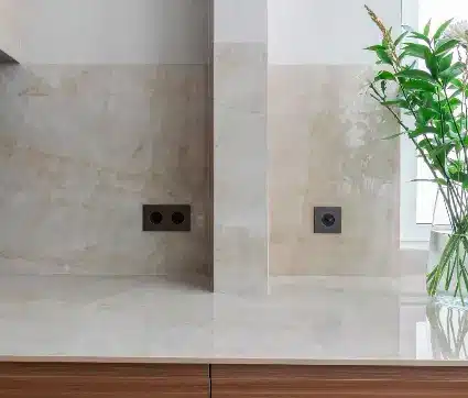 Dual black electrical outlets installed on a polished beige marble backsplash beside a potted plant. Dual black electrical outlets installed on a polished beige marble backsplash beside a potted plant.