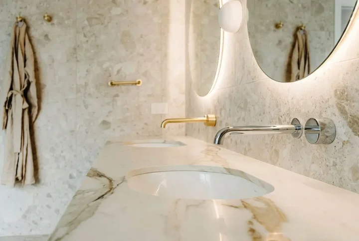 Shiny chrome and brass bathroom taps mounted on a marble countertop, with a circular mirror and soft lighting in a modern, elegant washroom. difference between chrome and brass taps integrated.
